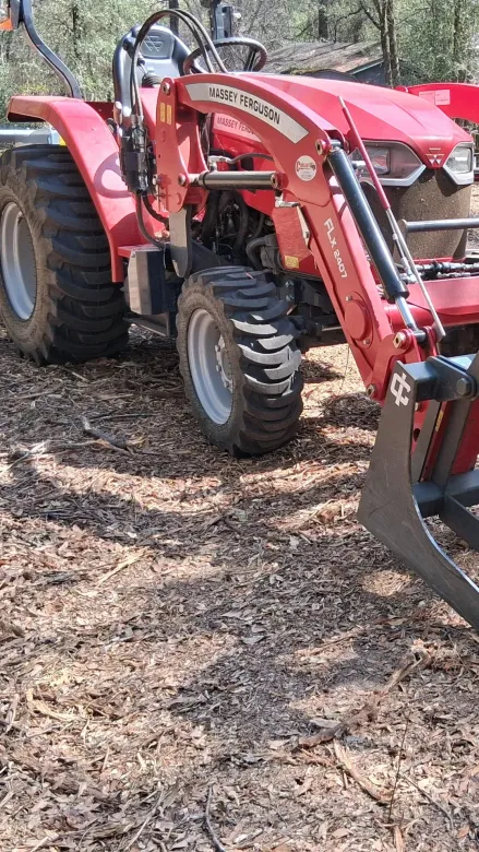 Red tractor with front loader on a dirt path in a wooded area