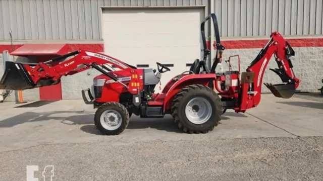 Red tractor with front loader and backhoe parked outside a metal building.