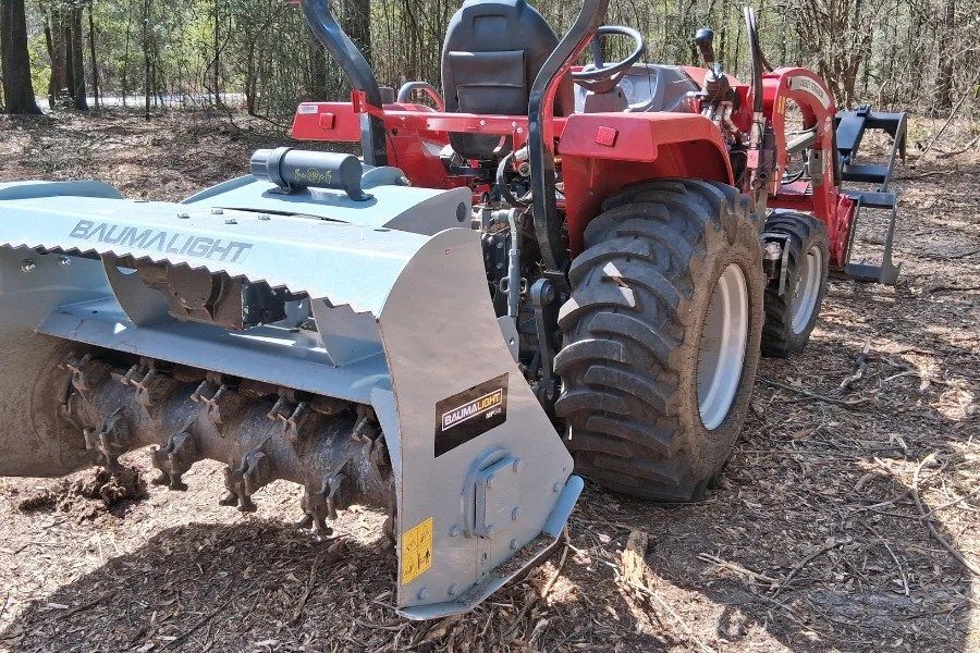 Red tractor with a front forestry mulcher attachment in a wooded area