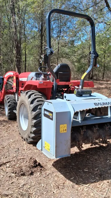 Red tractor with front mower attachment parked on a wooded dirt path