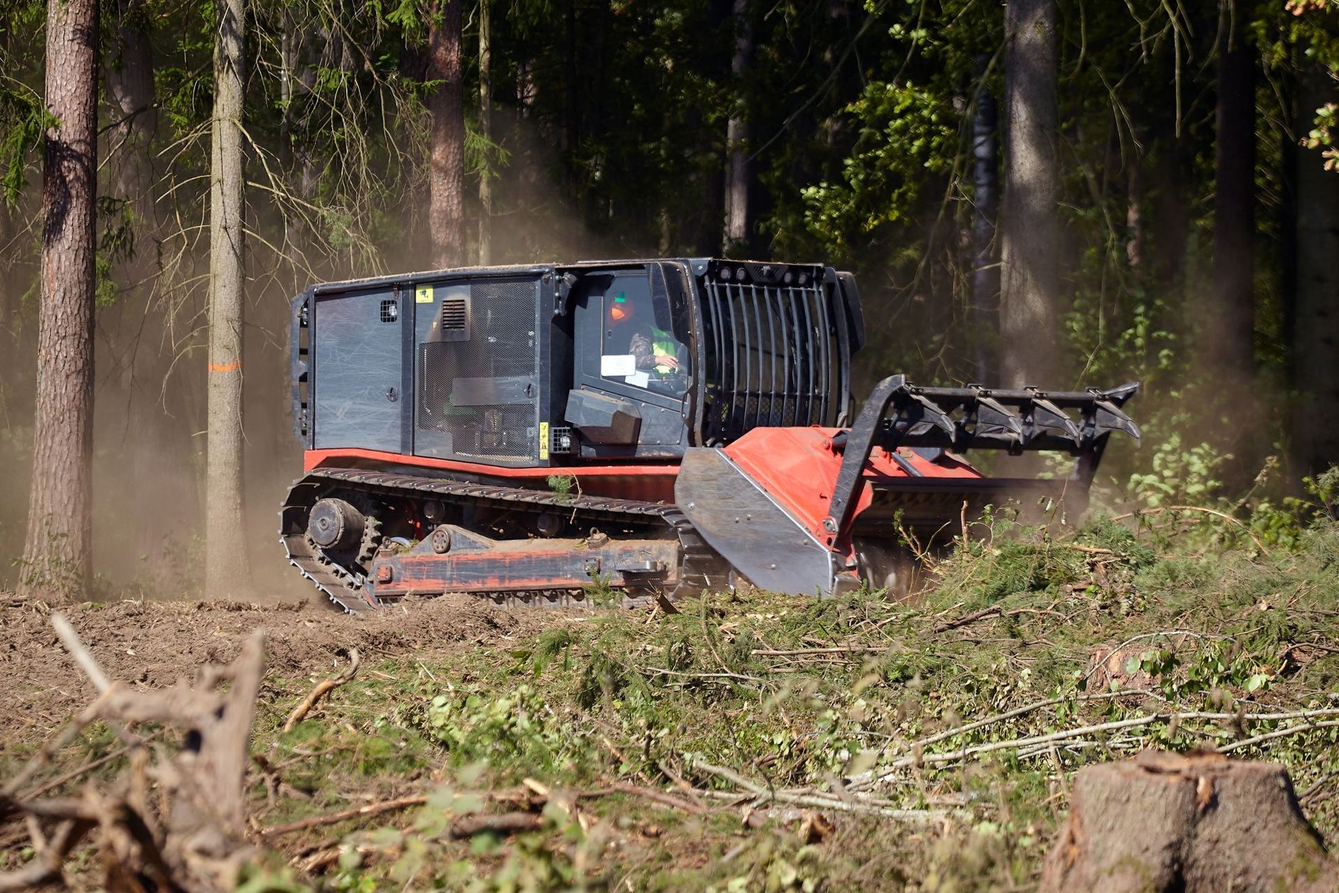 Tracked forestry mulcher clearing brush in a forest, kicking up dust and debris