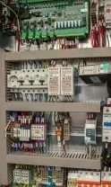 Interior of a gray electrical control cabinet featuring a green circuit board, circuit breakers, and organized wiring.