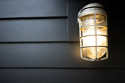 A lit cage-style outdoor wall sconce mounted on dark horizontal siding.