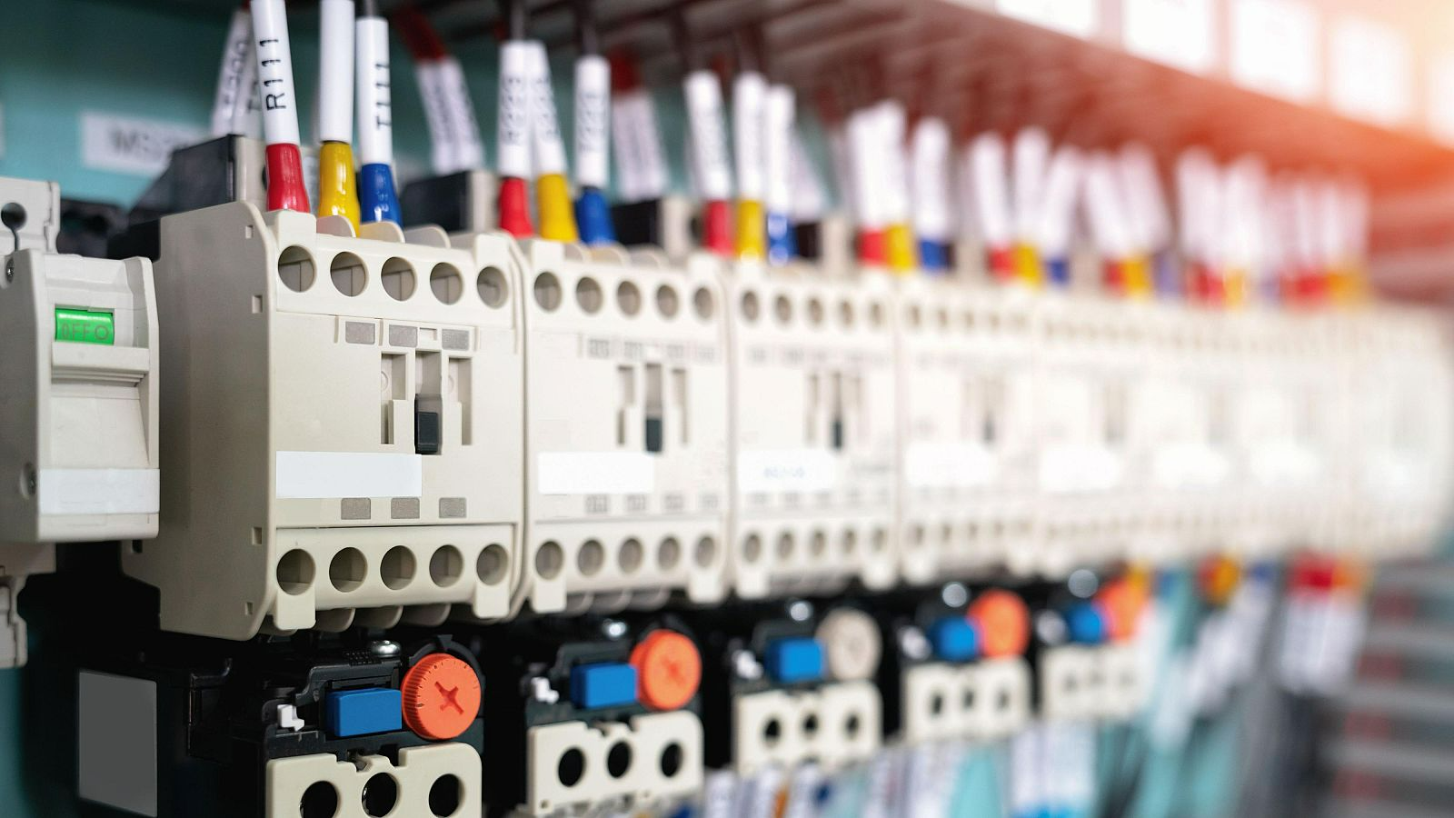 A row of electrical contactors with labeled wires connected to terminals inside a control panel.