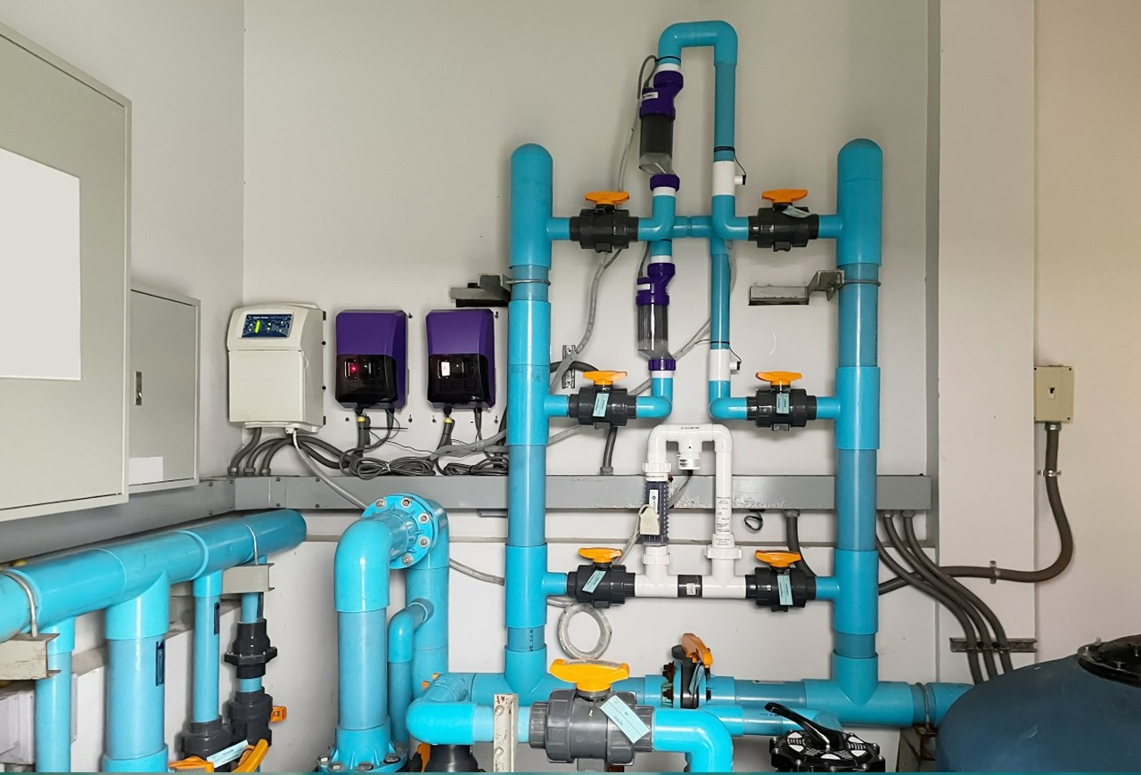 A complex network of blue PVC plumbing pipes, manual valves, and electronic controllers mounted on a wall in a utility room.