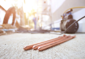 Three copper-coated grounding rods lie on a concrete surface in an outdoor construction area.