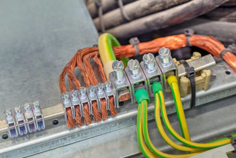 A grounding terminal block with multiple copper wires and green-and-yellow striped ground cables mounted on a metal rail.