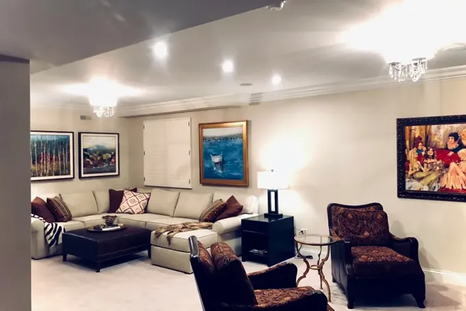 Elegant living room with beige sectional sofa, dark chairs, framed art, and soft ceiling lighting