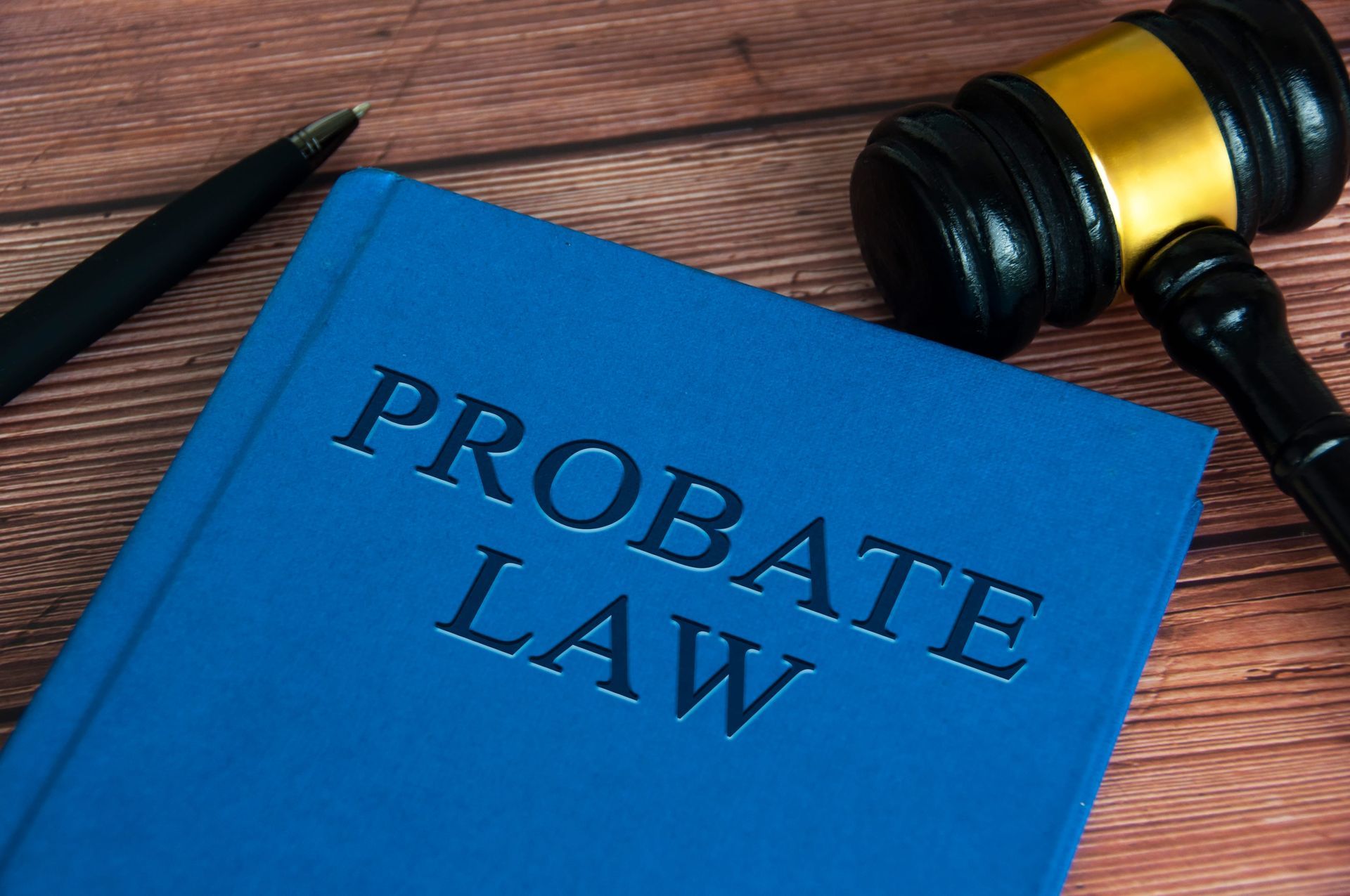Blue “Probate Law” book beside a gavel and pen on a wooden desk