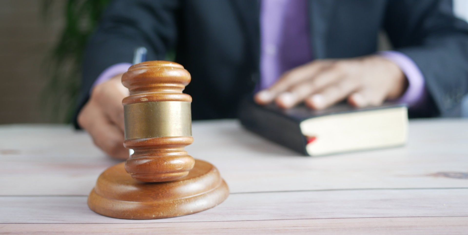 Wooden judge's gavel on a desk with a blurred person holding a book in the background