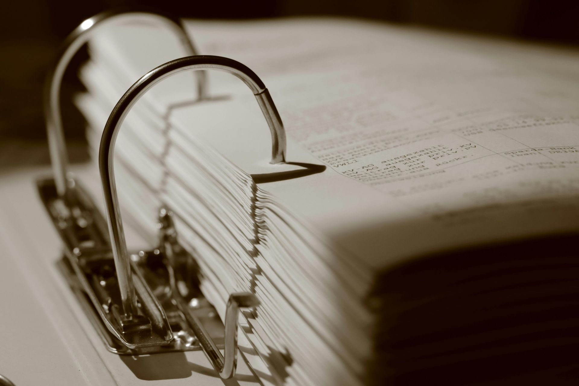 Sepia close-up of a metal binder clip holding a stack of pages with a book in the background