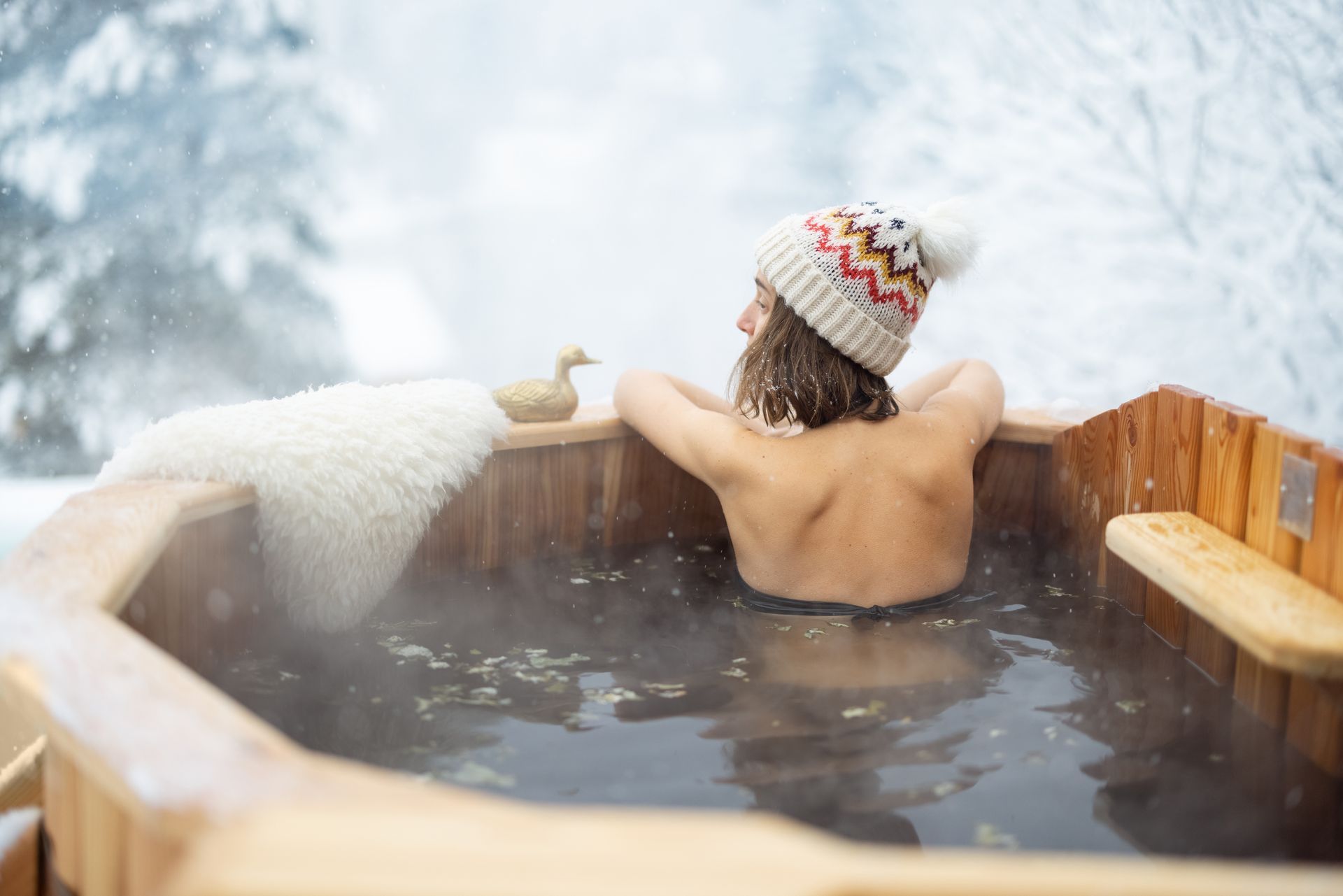 A woman is taking a bath in a wooden hot tub in the snow.