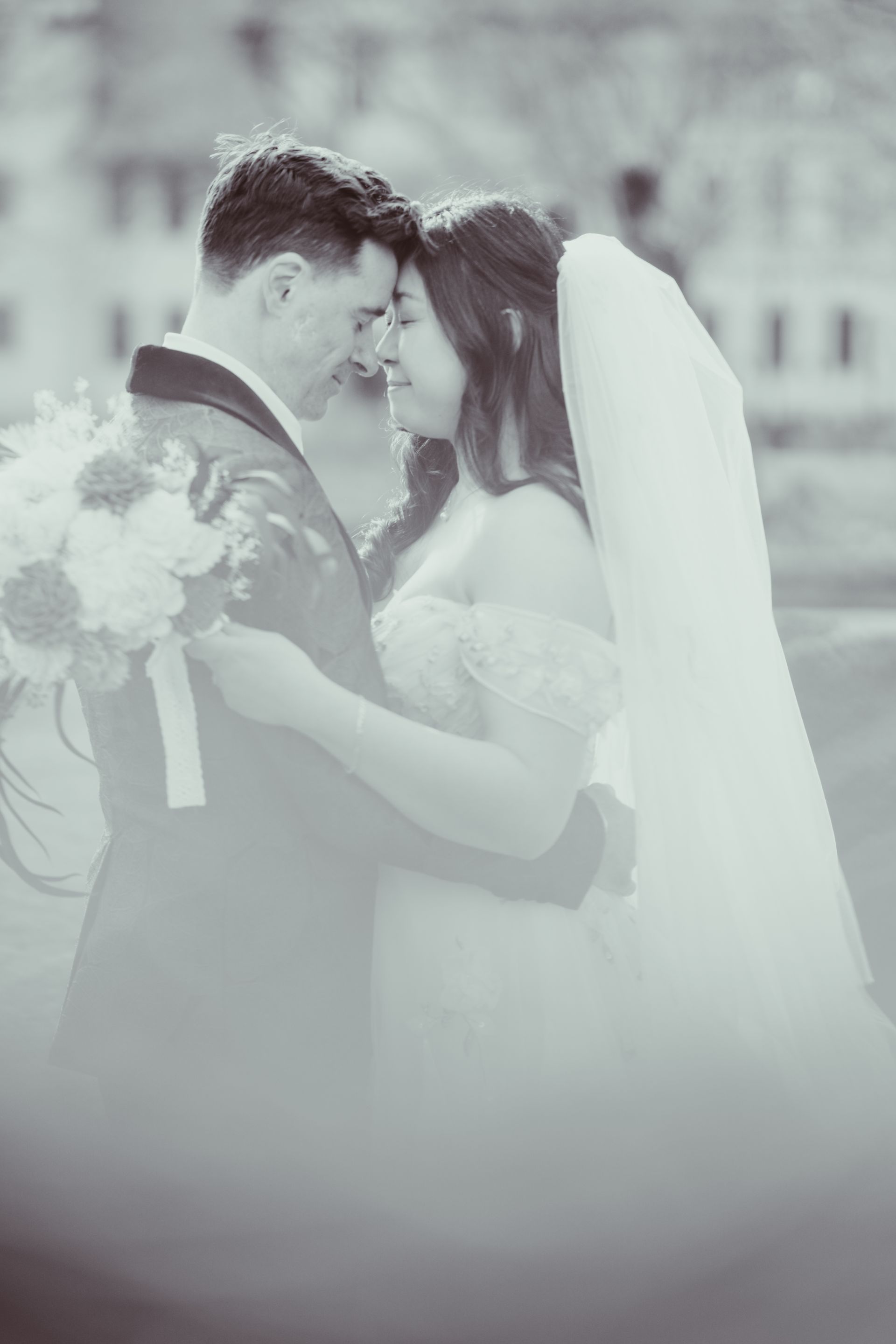 Wedding couple embracing and kissing, with the bride in a white veil holding a bouquet.