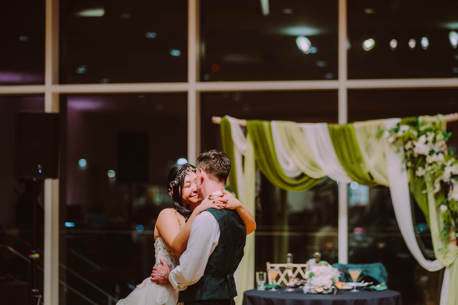 Couple embracing at a decorated wedding reception table by large windows at night