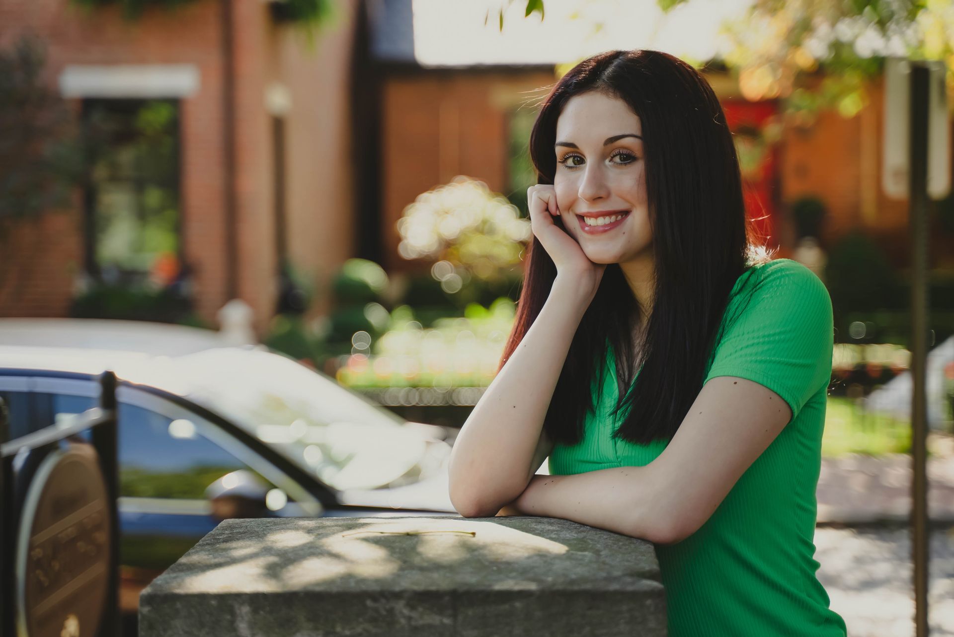 a woman in a green shirt is leaning on a stone wall .