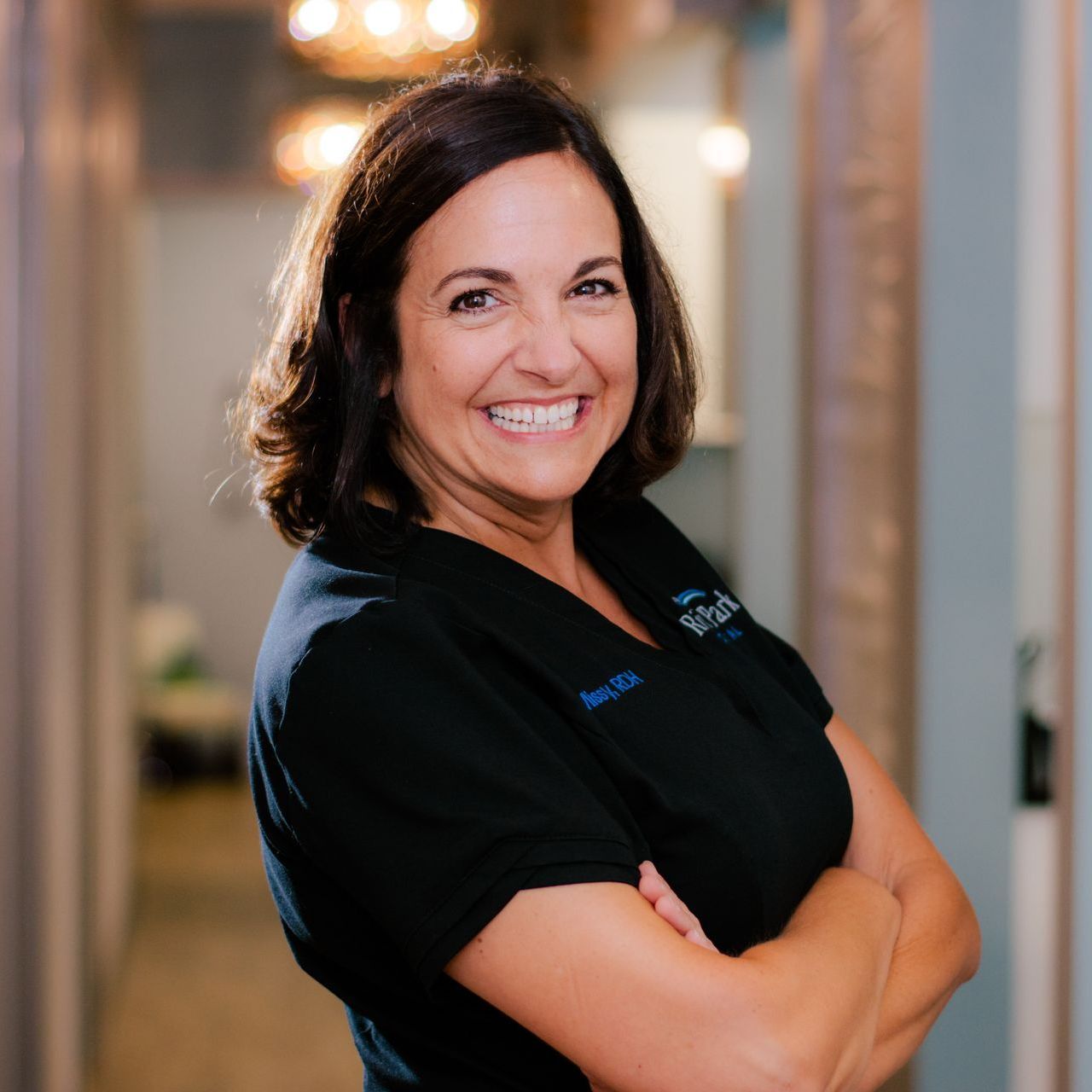 A woman in a black shirt is smiling with her arms crossed.