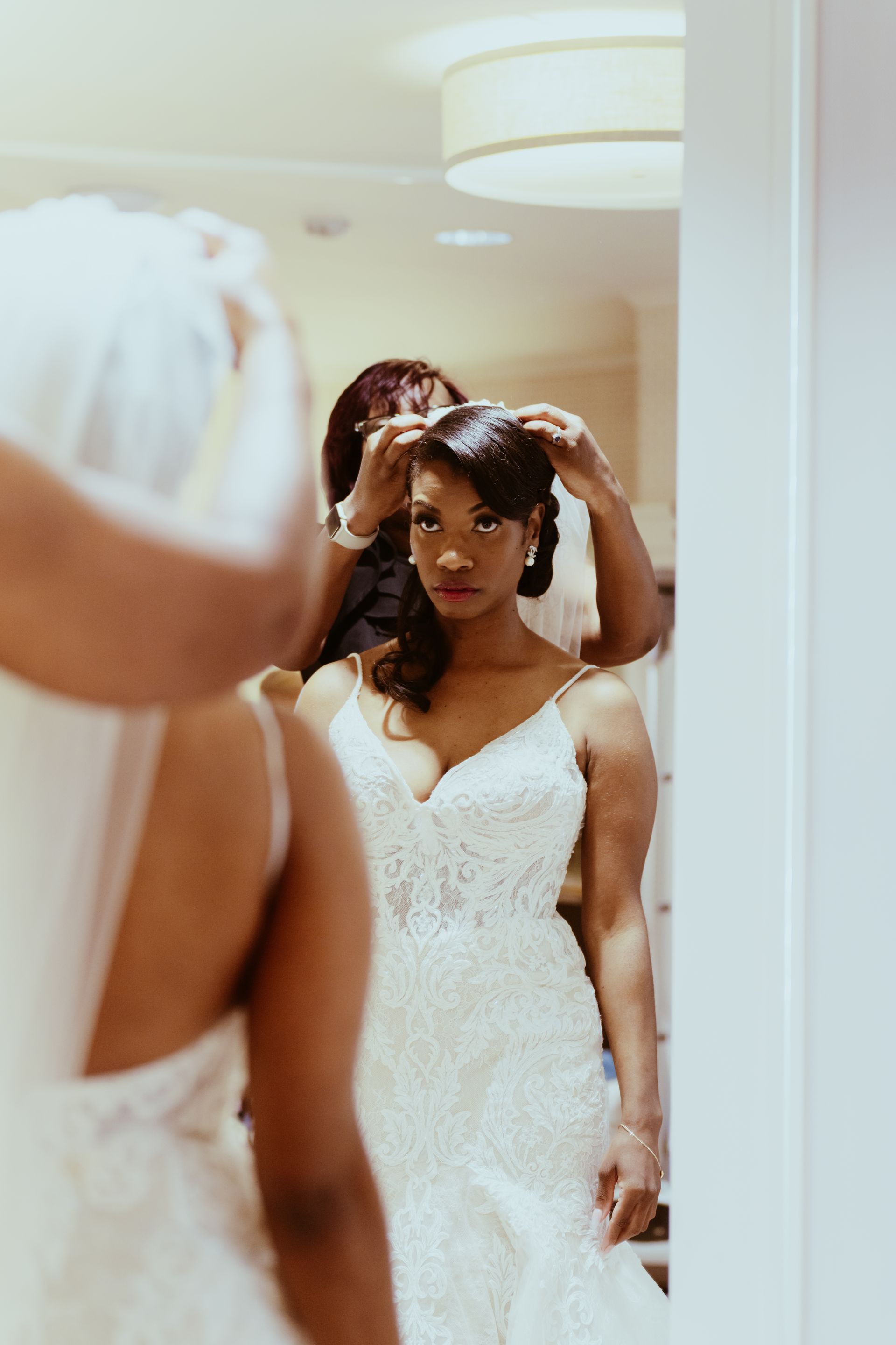 A woman in a wedding dress is getting ready in front of a mirror.