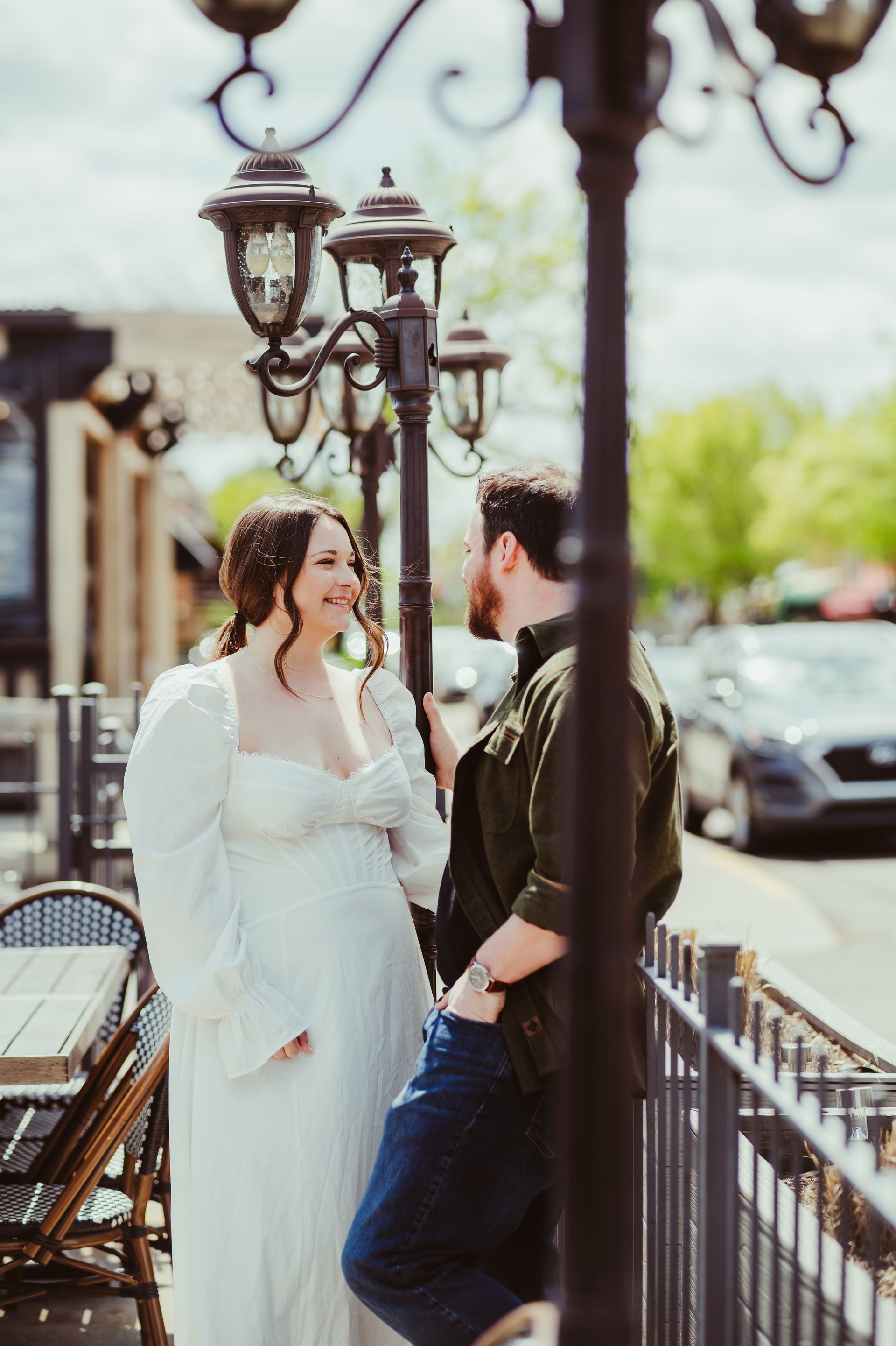 Couple posing and laughing on a street sidewalk beside café tables and ornate lampposts