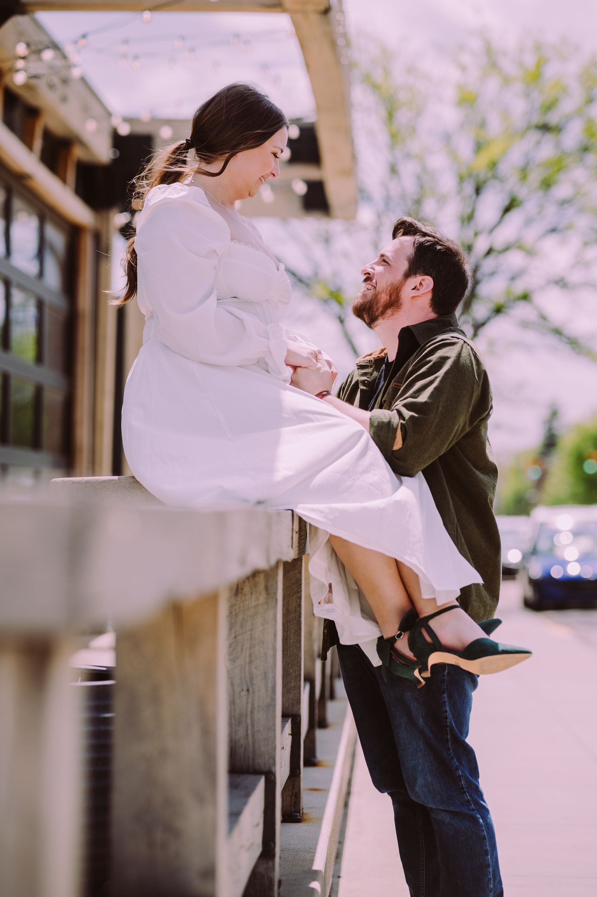 Couple embracing outdoors, with one person lifting the other beside a sidewalk and railing.
