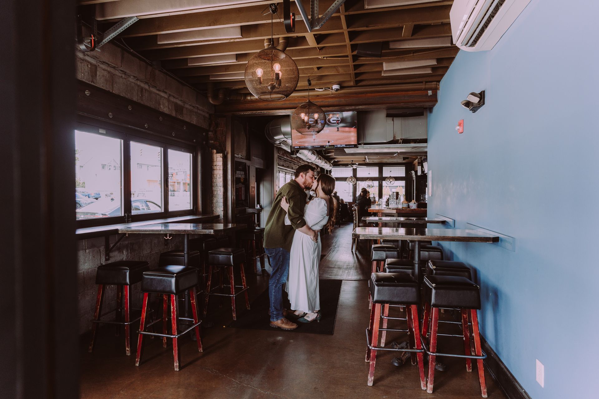 Two people standing in a narrow cafe with wooden beams, black stools, and a blue wall