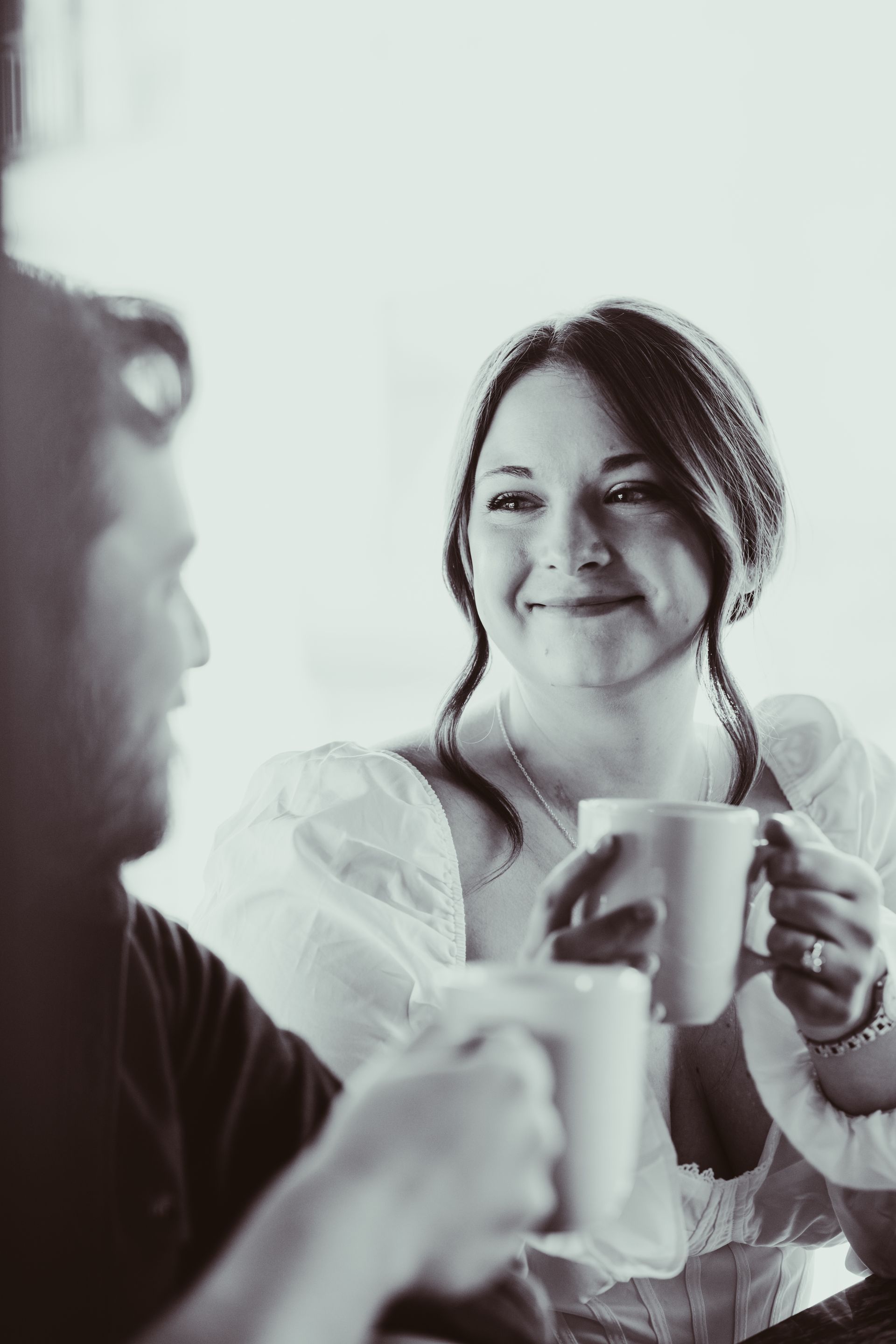 Two people chatting over coffee at a table, one smiling and holding a mug