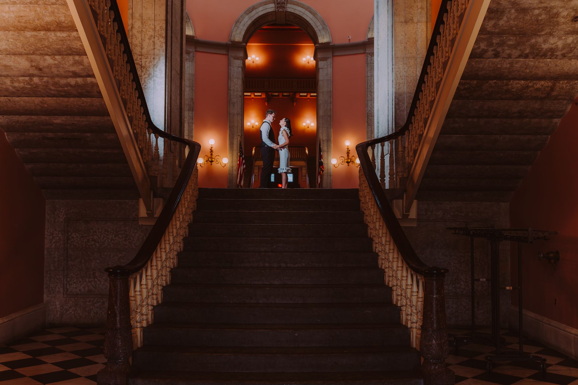 Grand staircase in a dimly lit, ornate hall with warm orange lights and a doorway at the top
