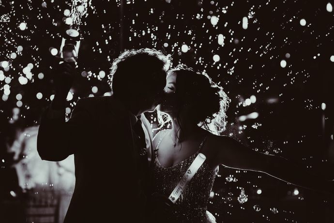 Couple kissing, silhouetted in falling confetti at night.