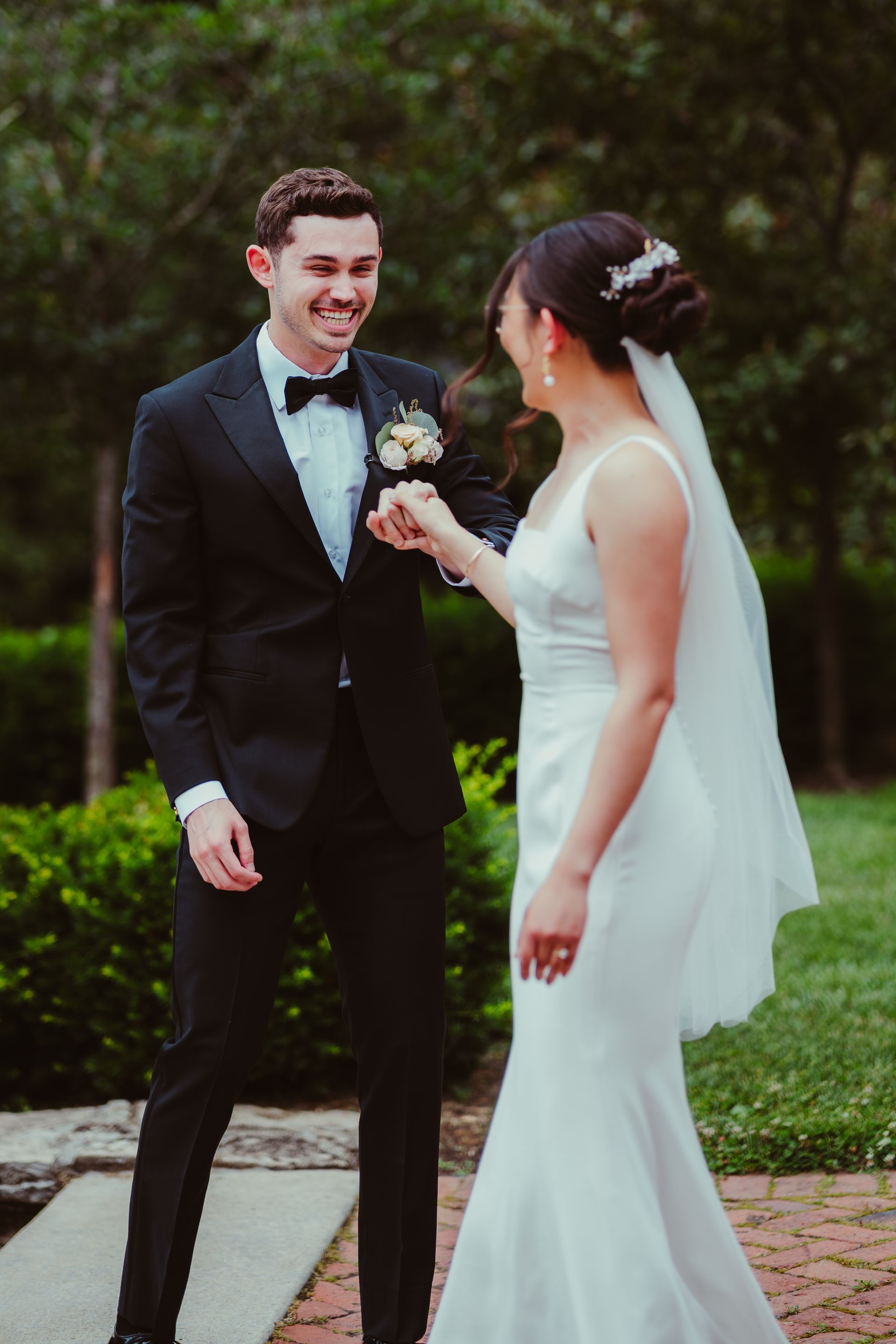 Bride and groom in wedding attire smiling and holding hands outdoors on a brick path