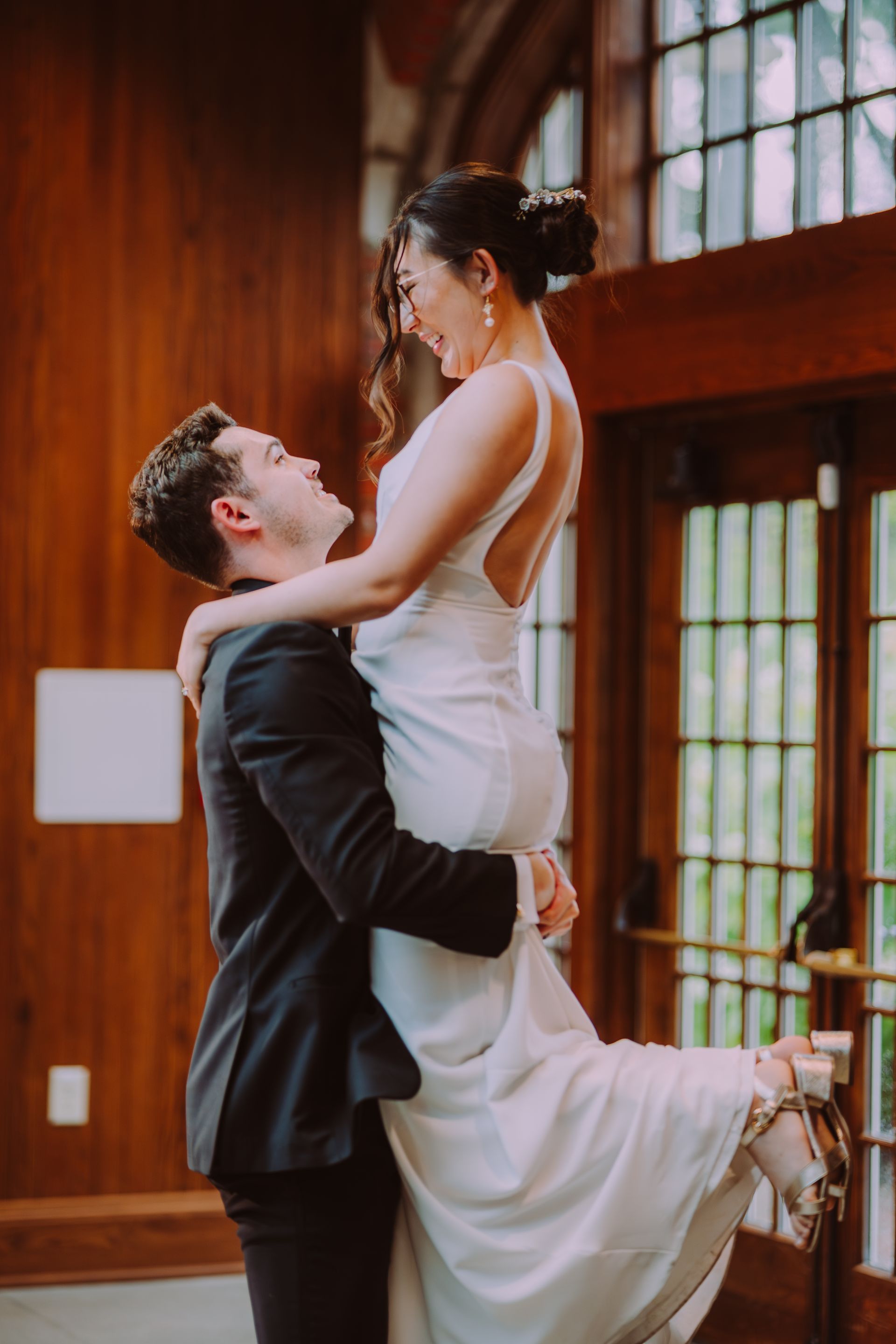 Couple in wedding attire embracing in a wood-paneled room with large windows