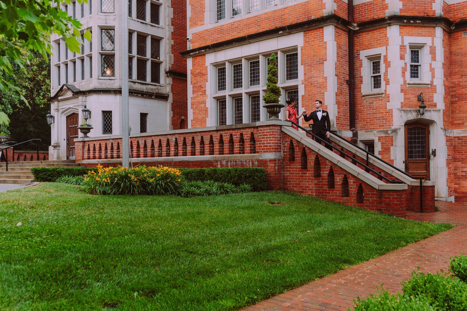 Brick building with white trim, staircase, and two people on the steps beside a green lawn