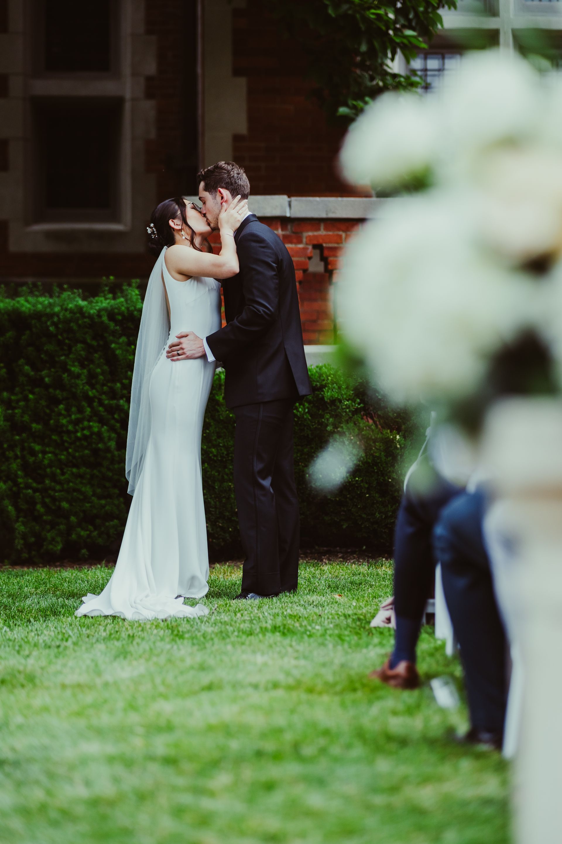 Wedding couple embracing on a lawn, with the bride in a white dress and groom in a dark suit.