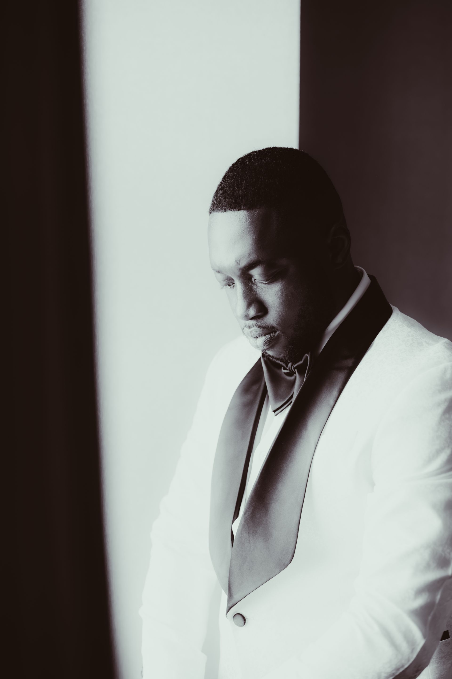 Man in a white suit looking down in a softly lit, high-contrast portrait