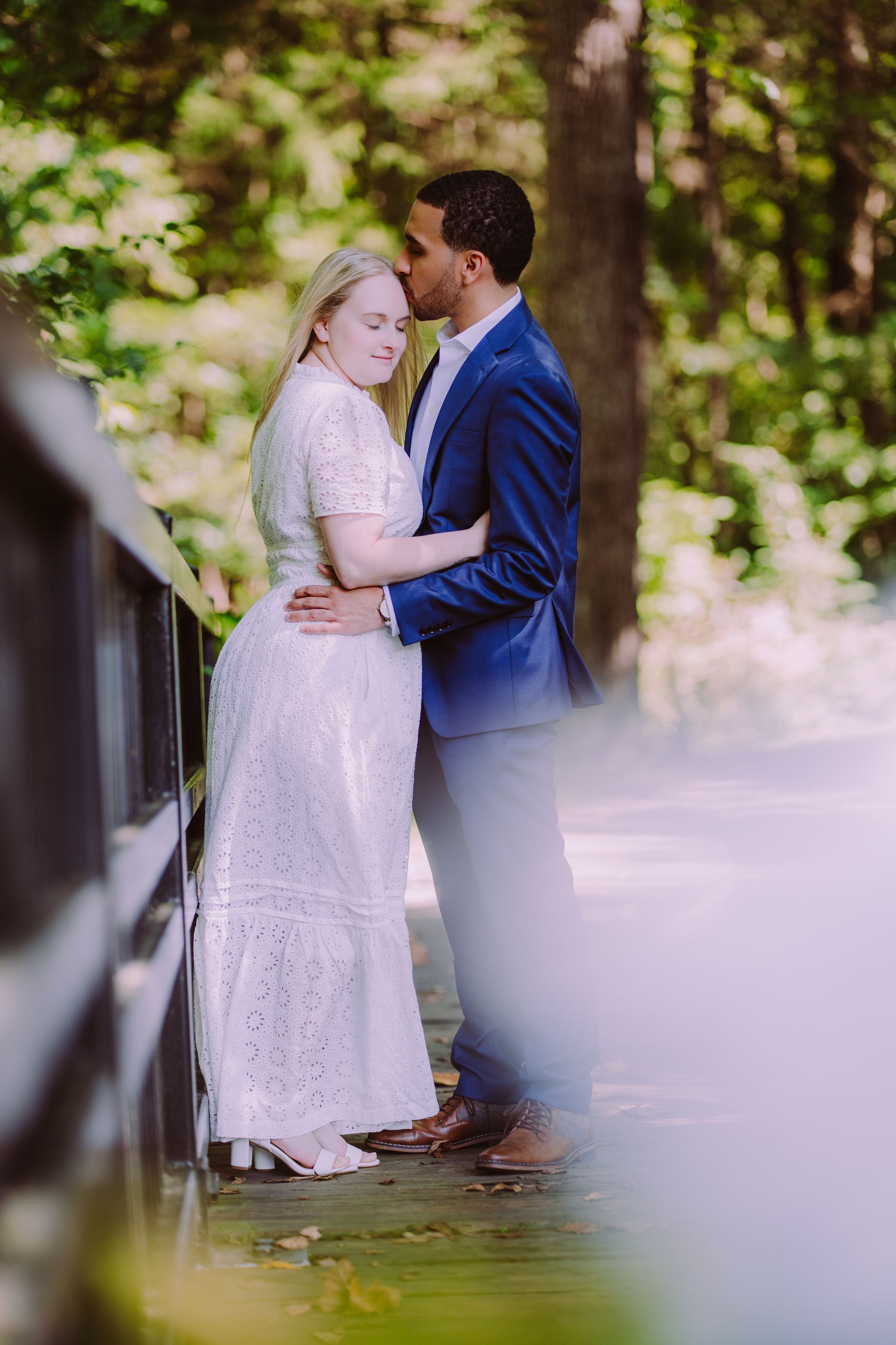 Two people embracing outdoors in a garden, with soft greenery and white flowers in the foreground.
