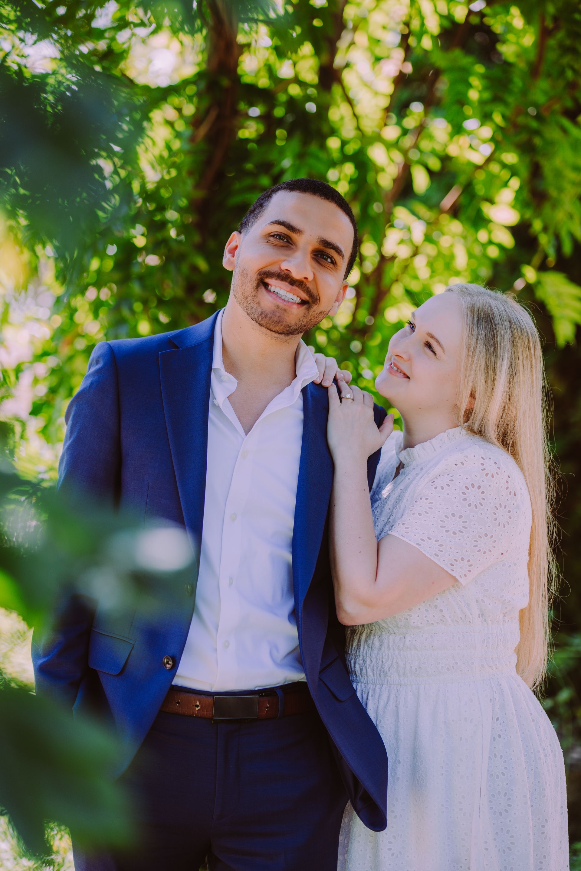 Smiling couple in blue and white outfits standing beneath leafy green trees