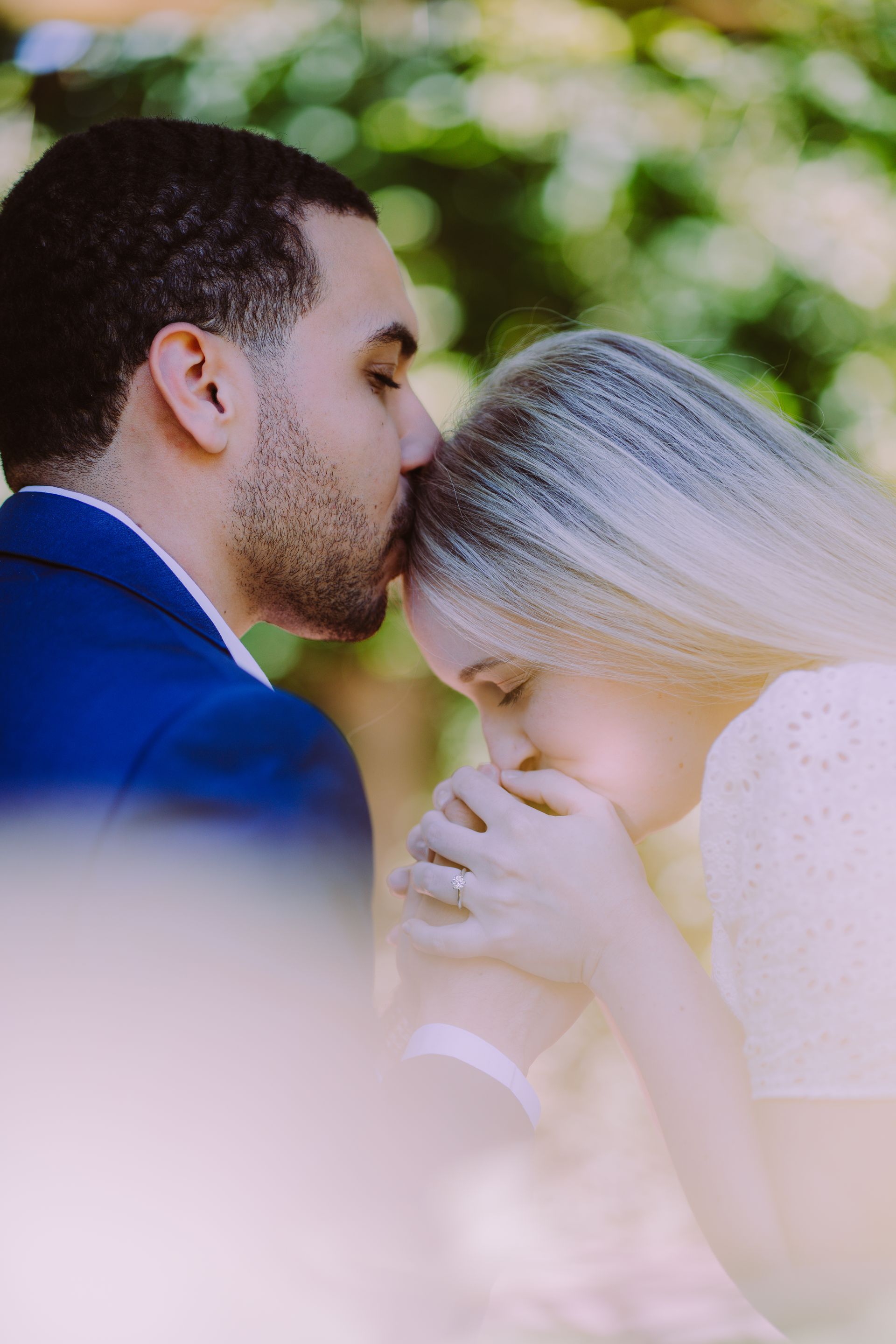 Couple kissing outdoors, with a white veil and soft green background.
