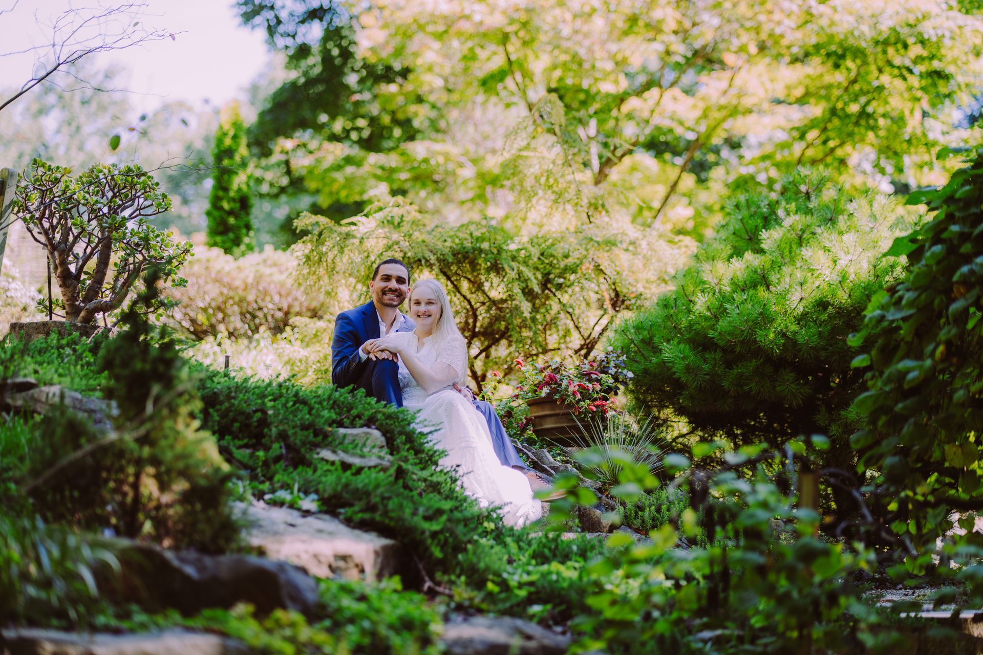 Bride and groom seated in a lush green garden under flowering trees