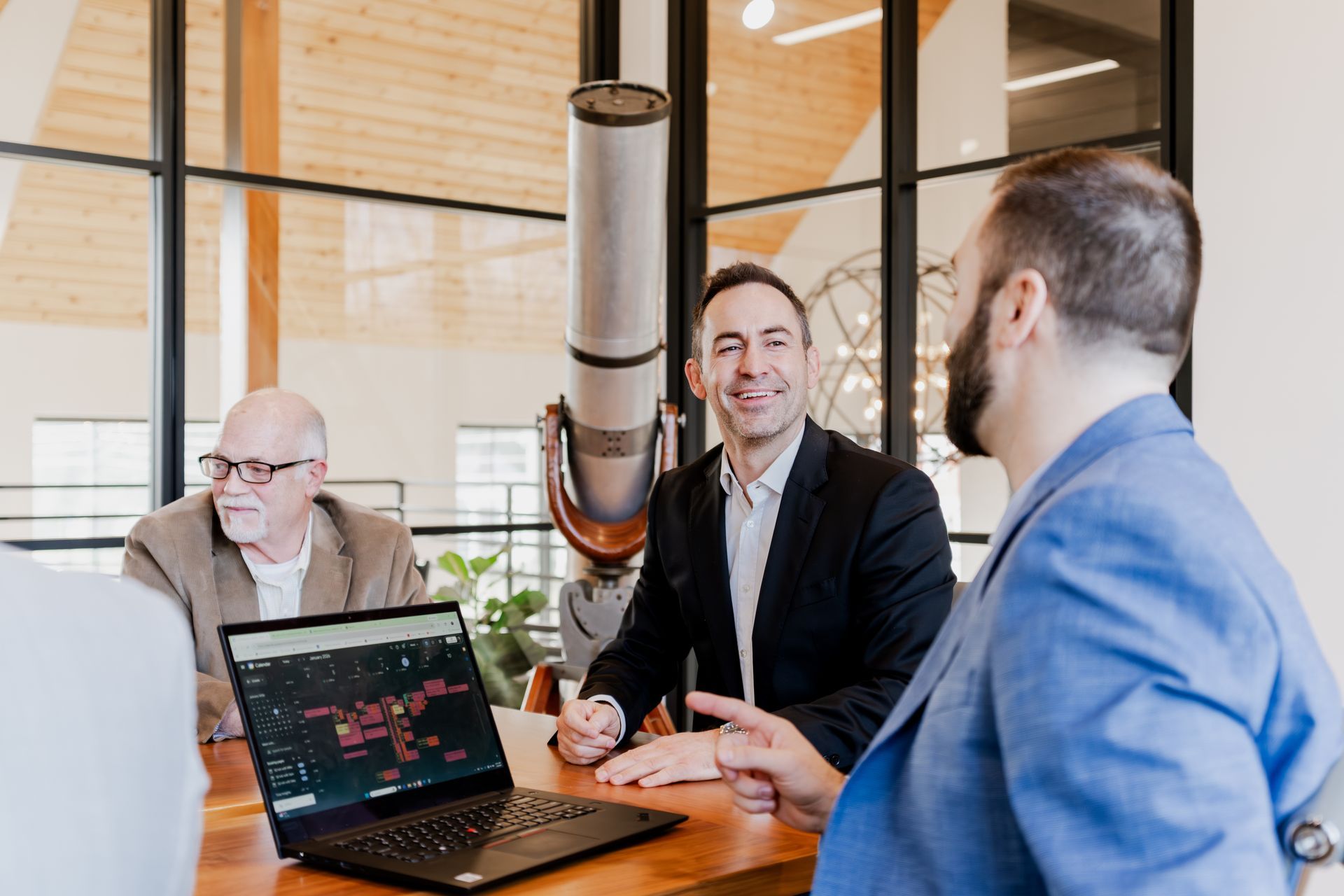 Four people in a meeting, one looking at a laptop with a graph, another talking, light-filled office.