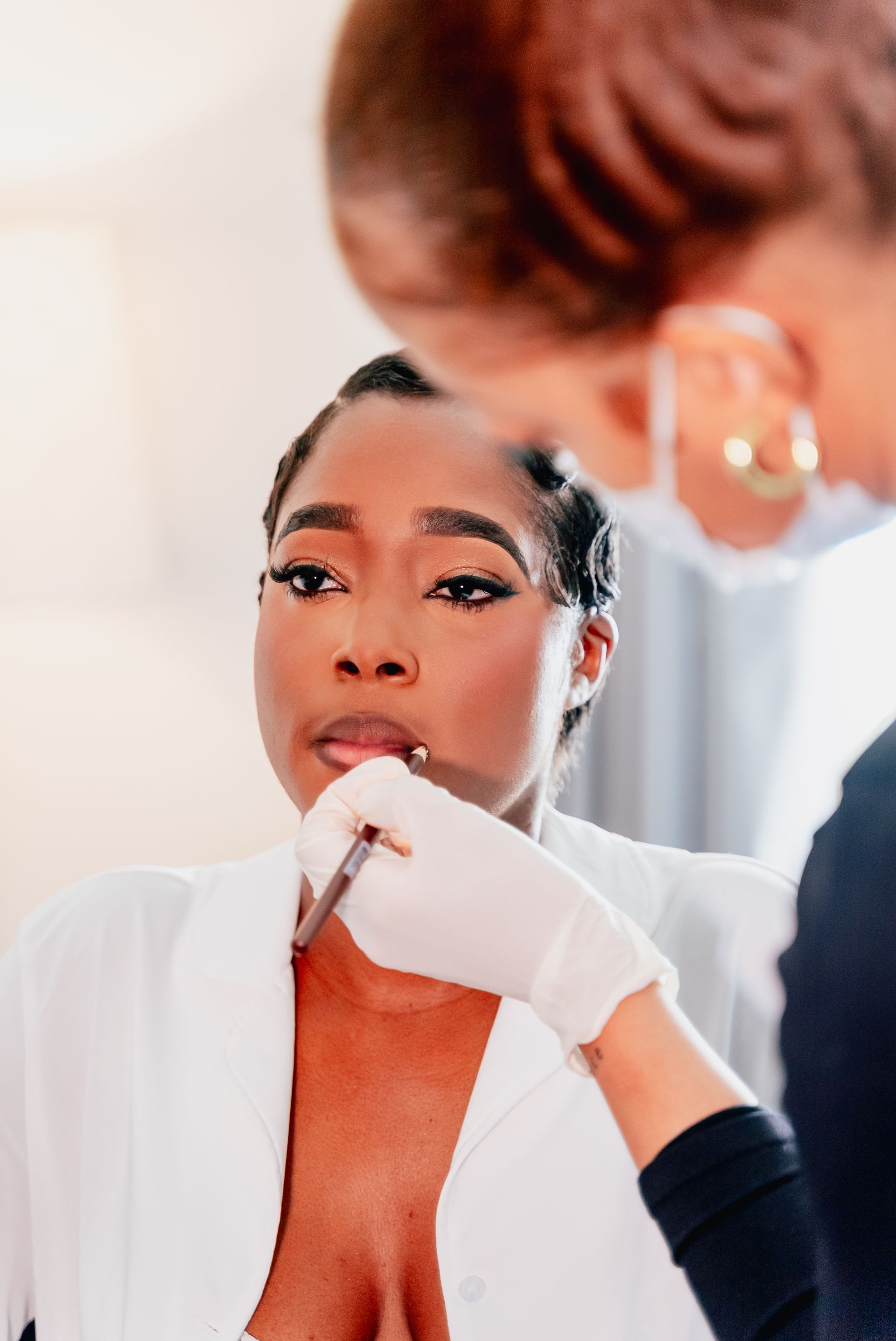 A bride is getting her makeup done by a makeup artist in front of a mirror.