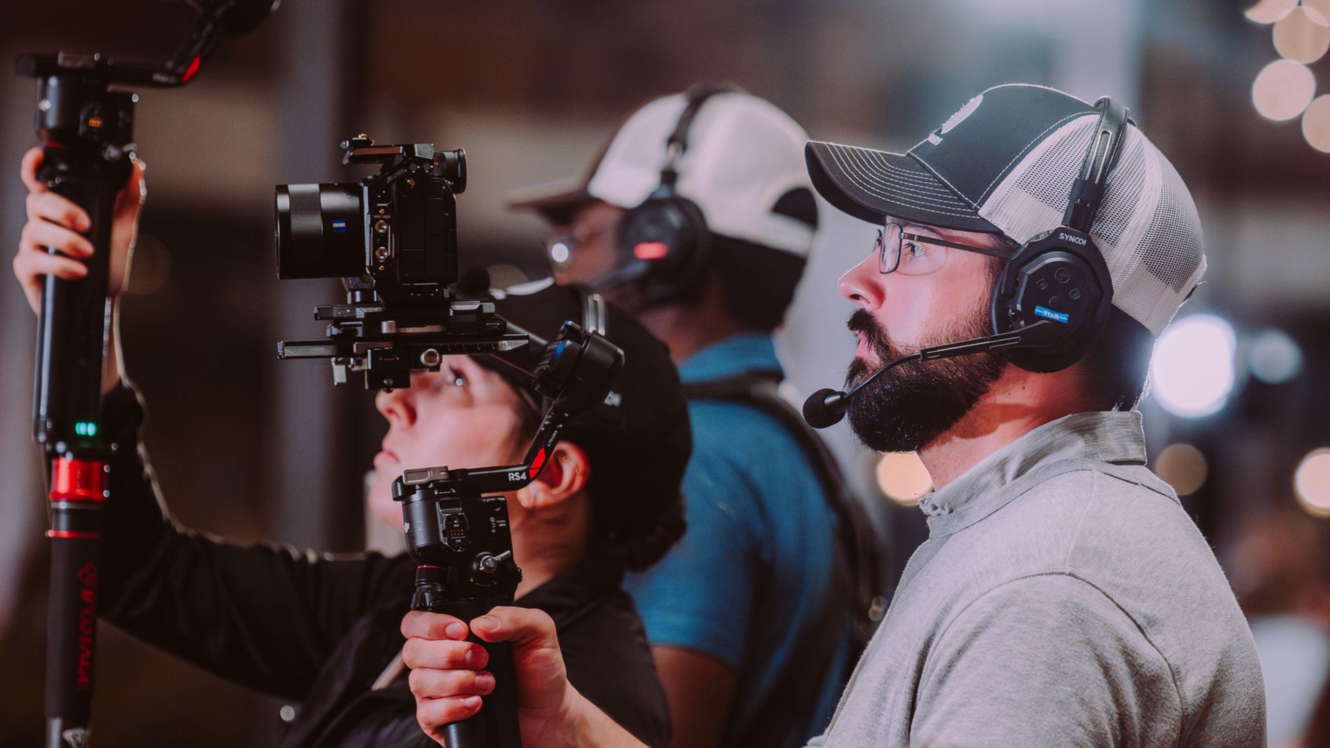 Camera crew wearing headsets filming on a gimbal at night, with blurred city lights in the background