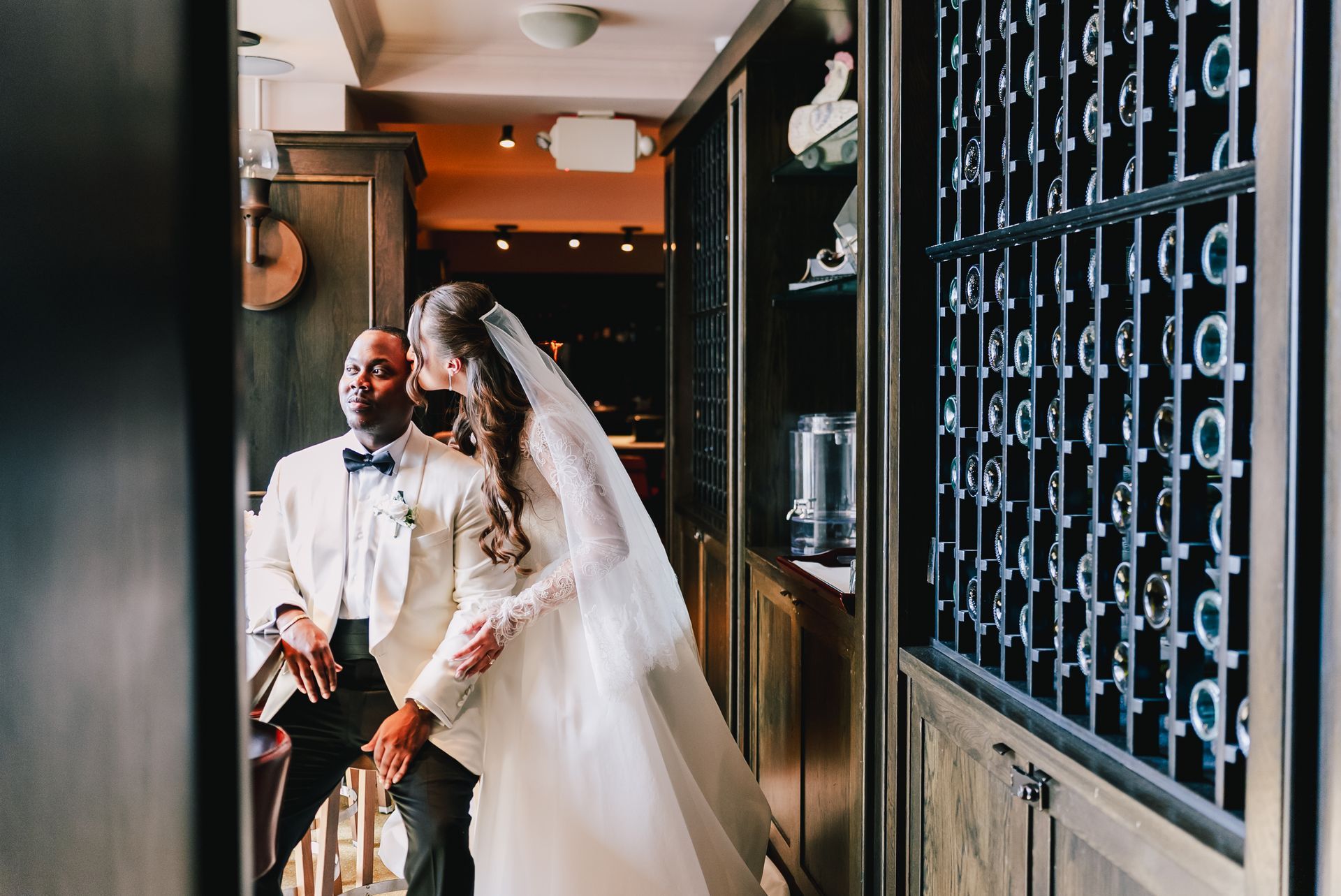 Bride and groom posing in a narrow hallway with wine racks and warm lighting