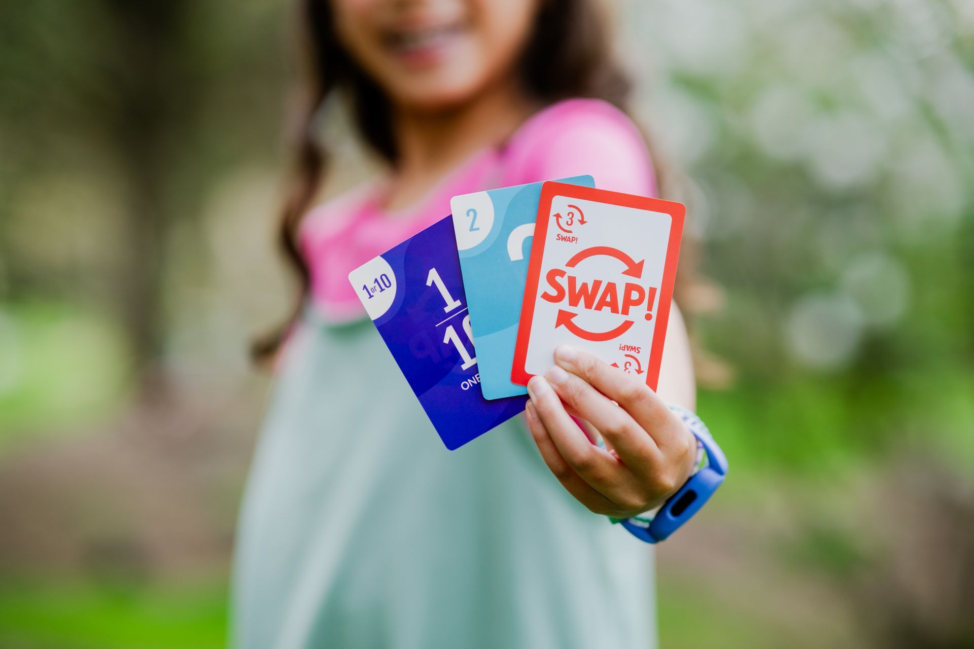 Hand holding three colorful swipe cards outdoors, with a blurred person in the background