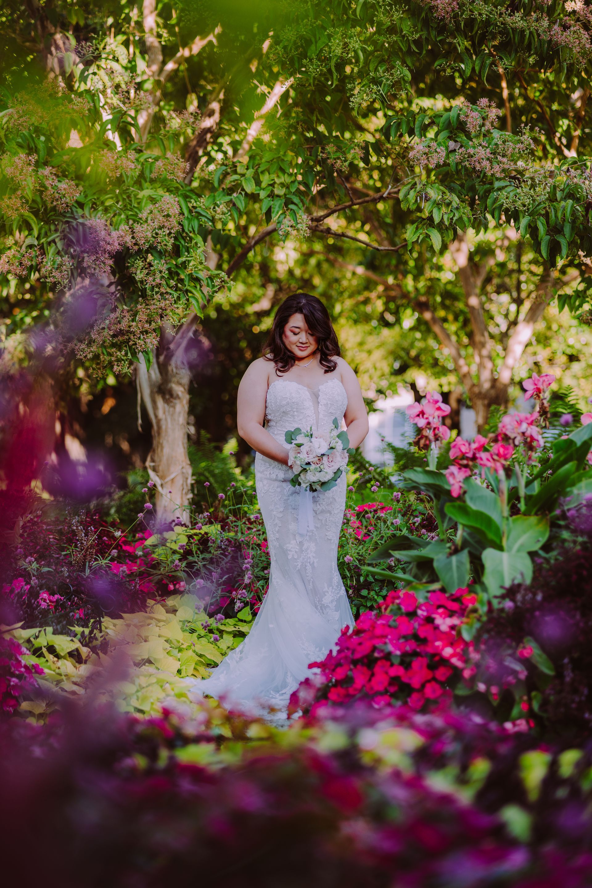 Bride in white dress holding bouquet in a lush, floral garden.