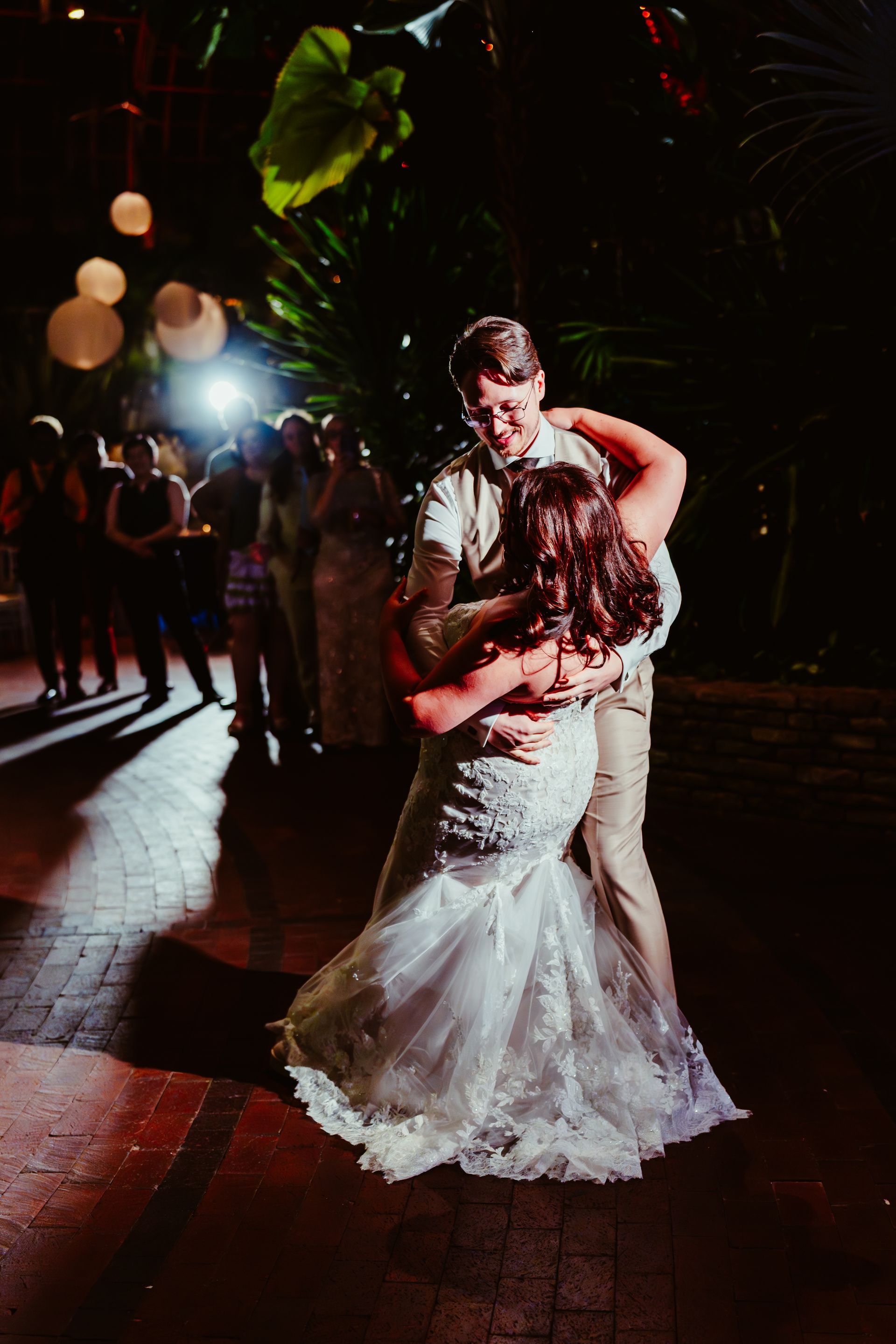 Newlyweds share a romantic dance, embraced in a wedding venue at night, surrounded by guests. Photo by Kodjo somana