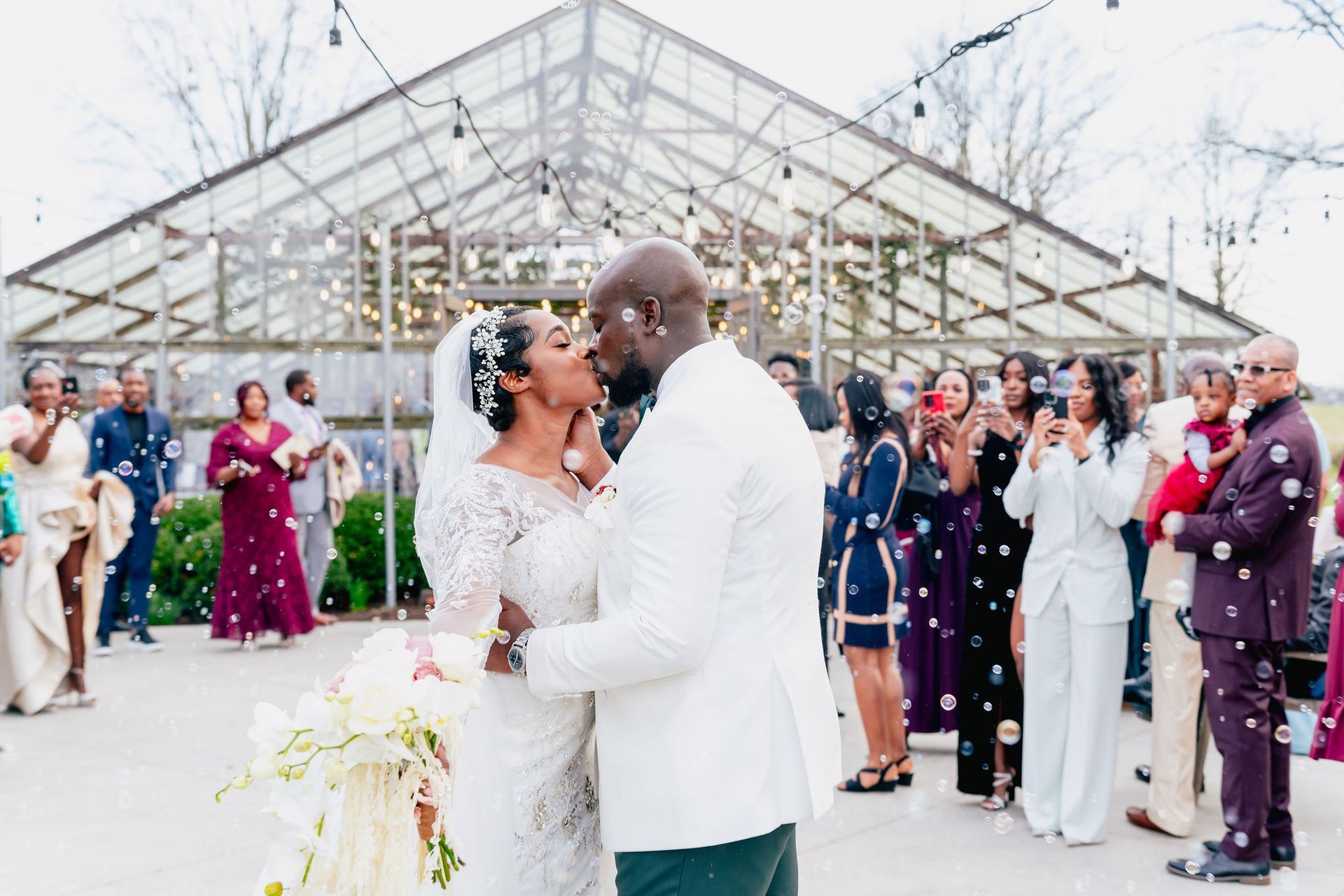 A bride and groom are kissing in front of their wedding guests.