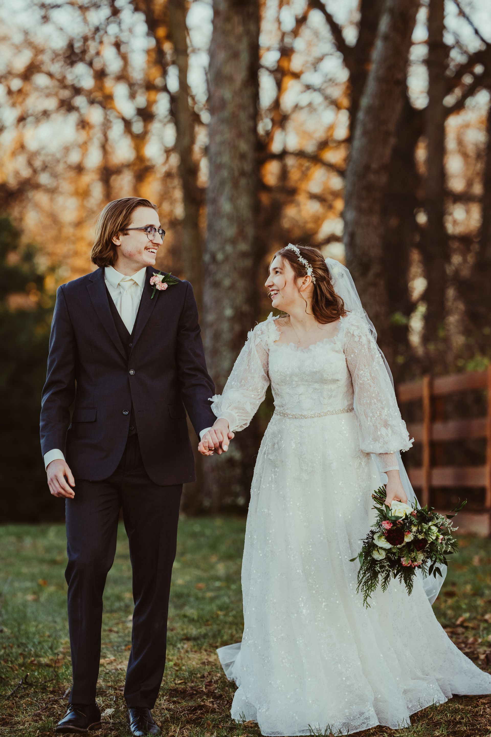A bride and groom are holding hands while walking through a field.