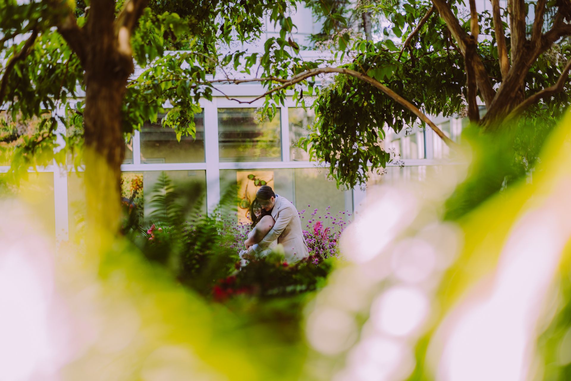 Couple embraces outdoors, framed by greenery;  at Franklin Park Conservatory in columbus