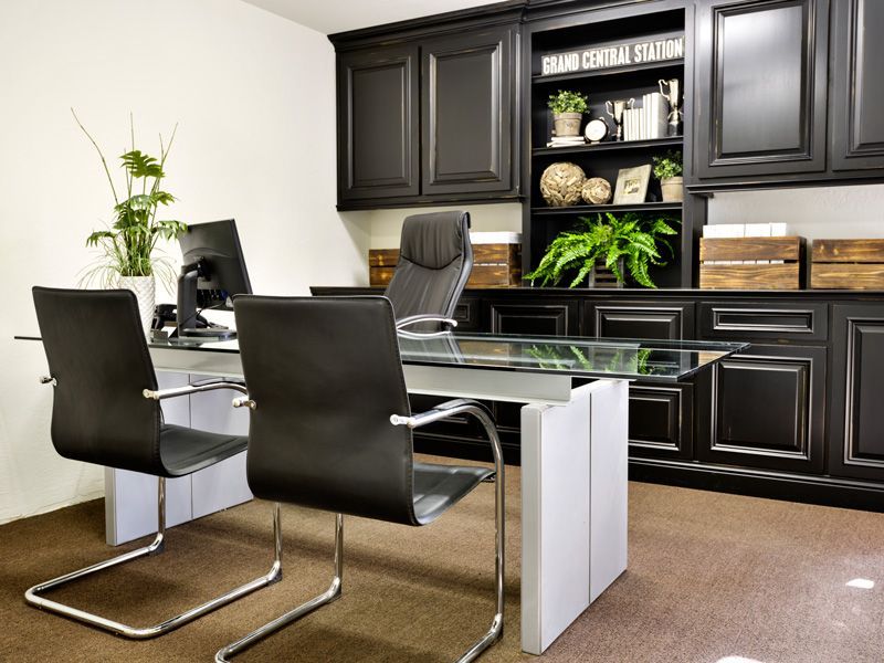 Modern office with black leather chairs, glass desk, and dark cabinets with plants and decor