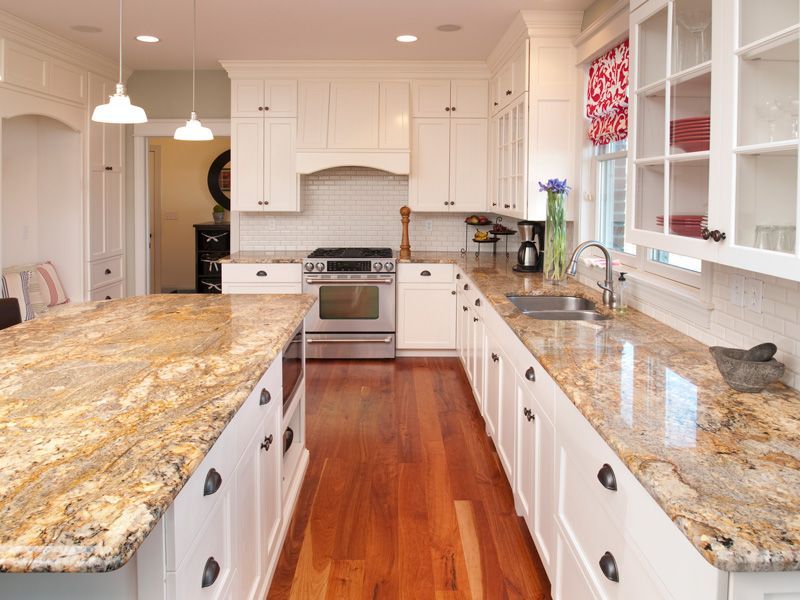 Bright kitchen with white cabinets, granite island, stainless stove, and hardwood floors