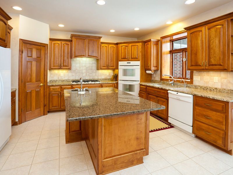 Spacious kitchen with cherry cabinets, granite island, white tile floor, and built-in oven and dishwasher