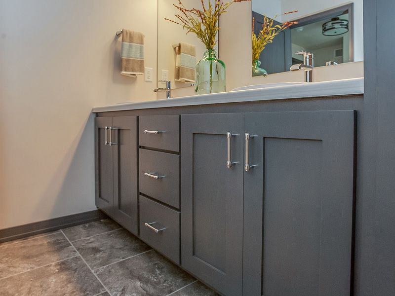 Modern bathroom vanity with gray cabinets, white countertop, and mirror over tiled floor.